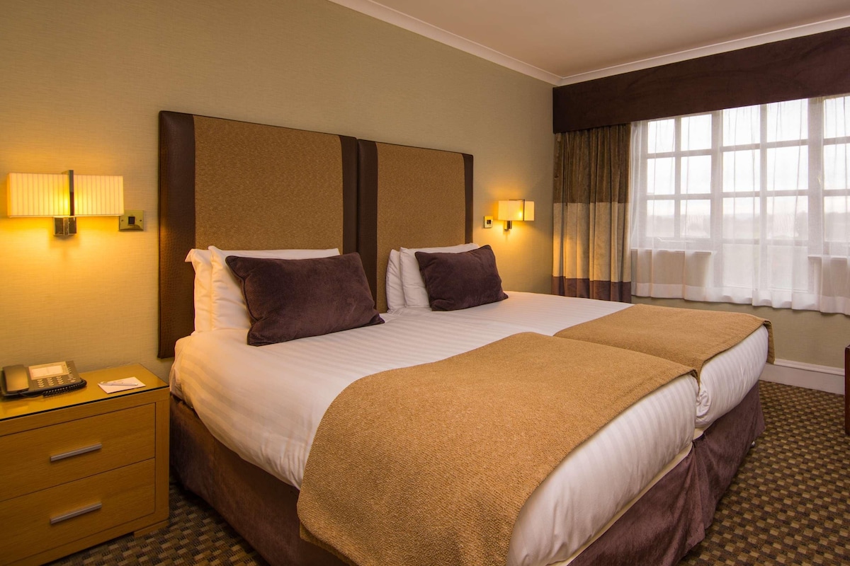 A hotel room with two beds, a desk, a chair, and a window with curtains.