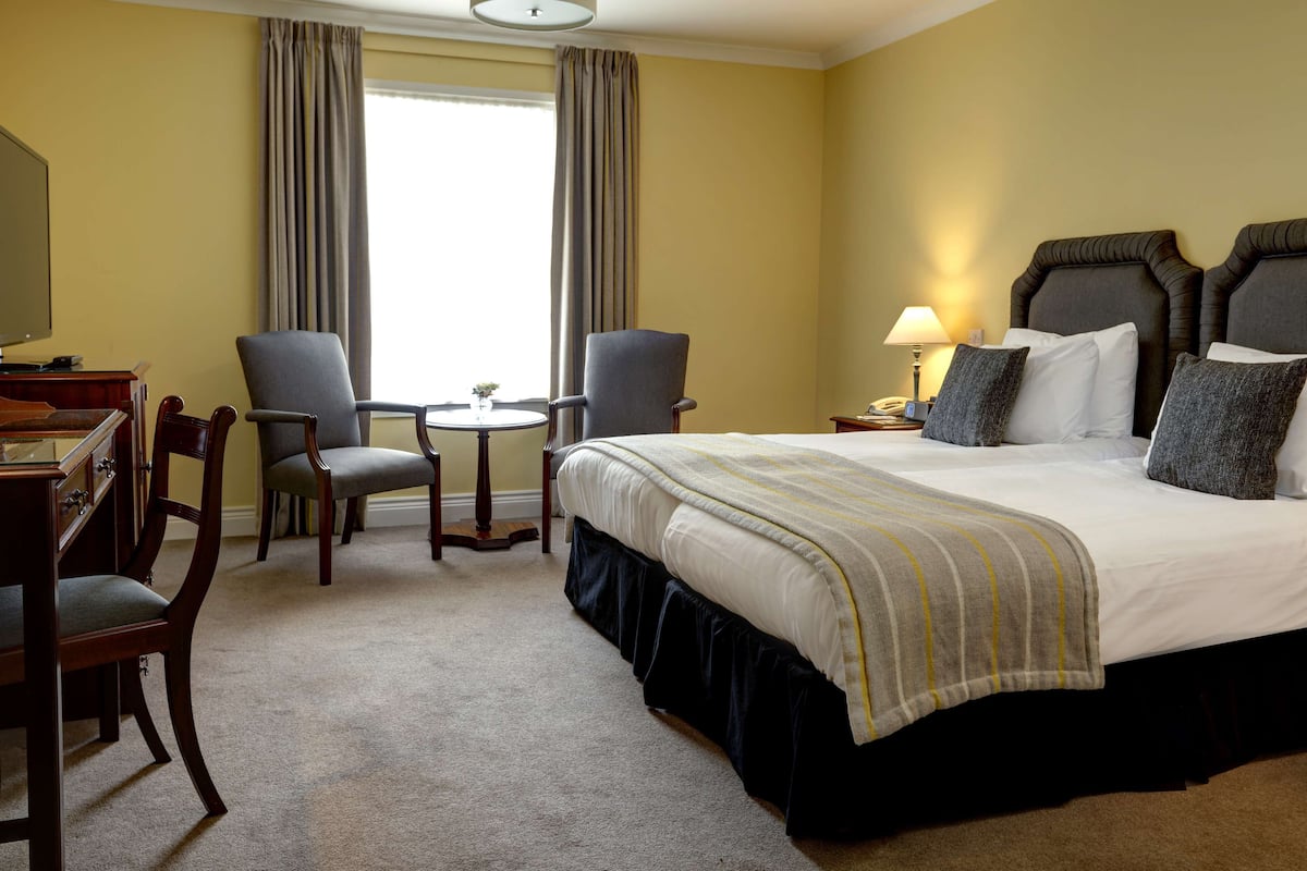 Una habitación de hotel con una cama grande, dos sillones, un escritorio y una mesita.
