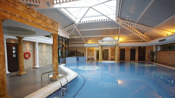 An indoor swimming pool with a skylight ceiling, columns, and a brick wall.