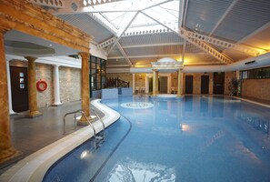 Una piscina interna con soffitto in vetro, colonne e parete in mattoni.