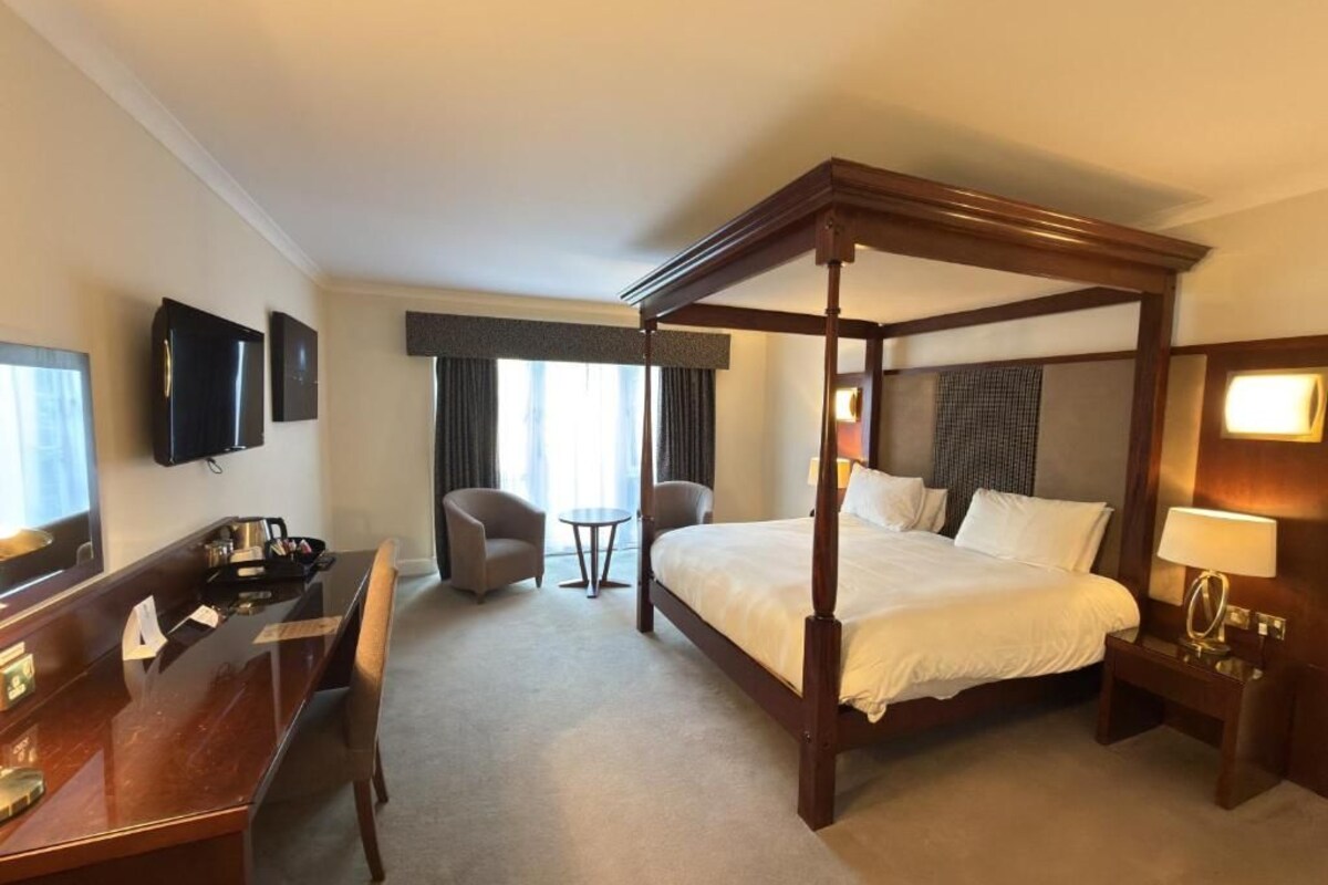 A four-poster bed in a hotel room with a desk, chair, and television.