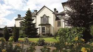 A large, stately building with a symmetrical facade, a prominent central window, and a well-maintained garden with various flowering plants.