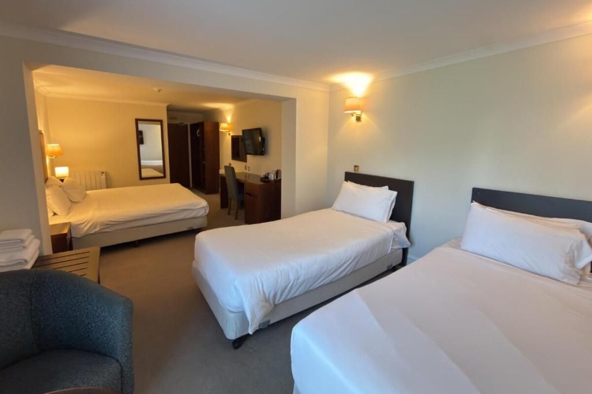 A hotel room with two beds, a desk, a chair, and a television.