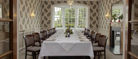A conference room with a long table set for a meeting, surrounded by chairs, with a large window and a chandelier.