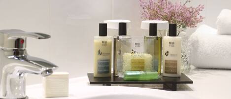 A bathroom sink with toiletries including a bar of soap, three bottles of Keju bath salts, and a green bar of soap.