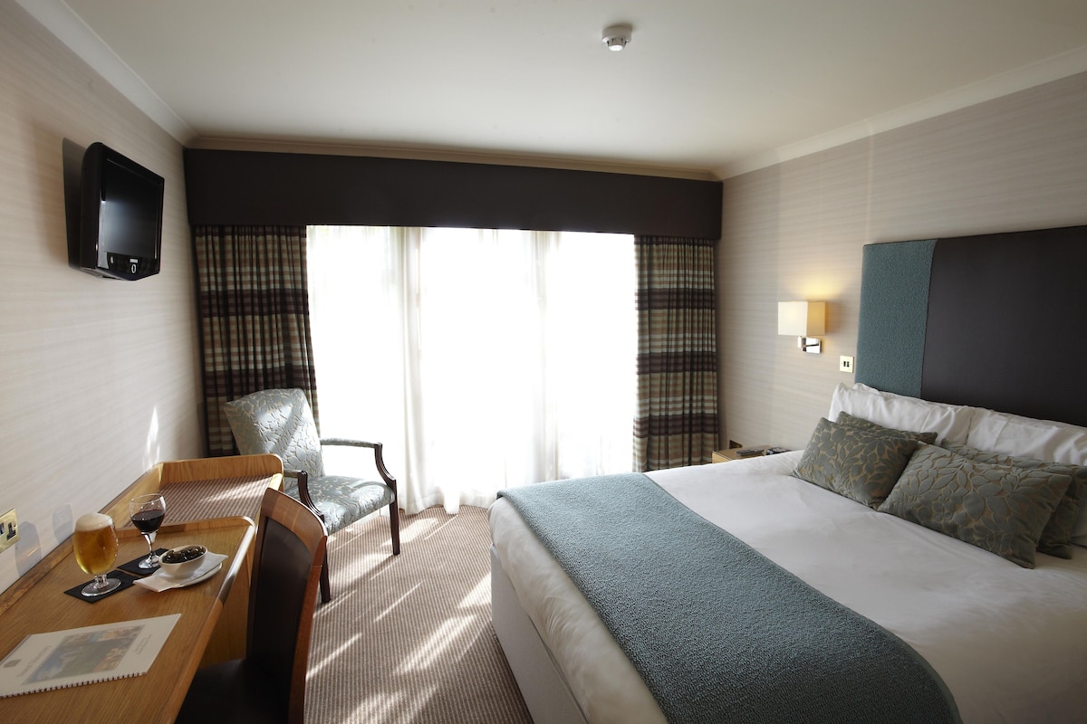A hotel room with a bed, a desk with a chair, a television, and a window with curtains.