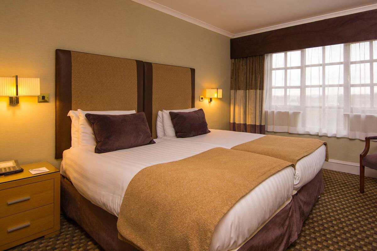Habitación de hotel con dos camas, un escritorio, una silla, un teléfono y lámparas.