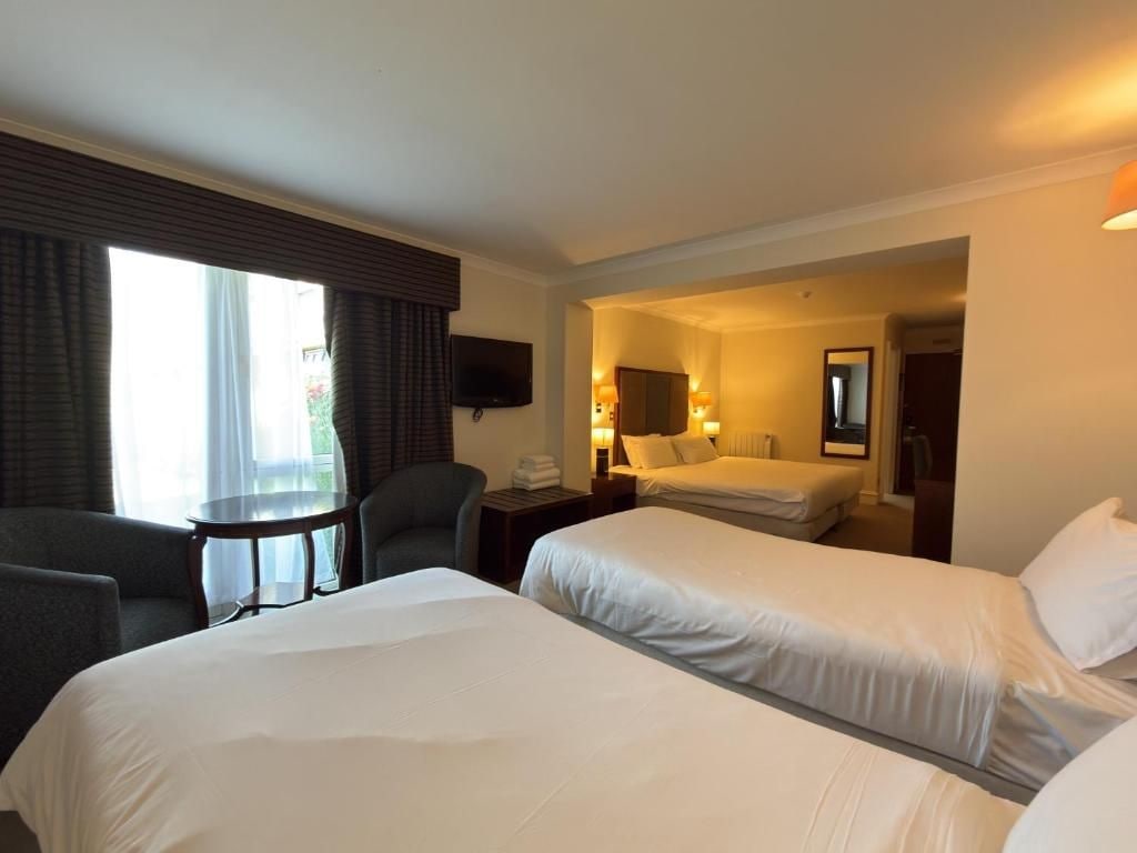 A hotel room with two beds, a desk, a chair, a TV, and a window with curtains.
