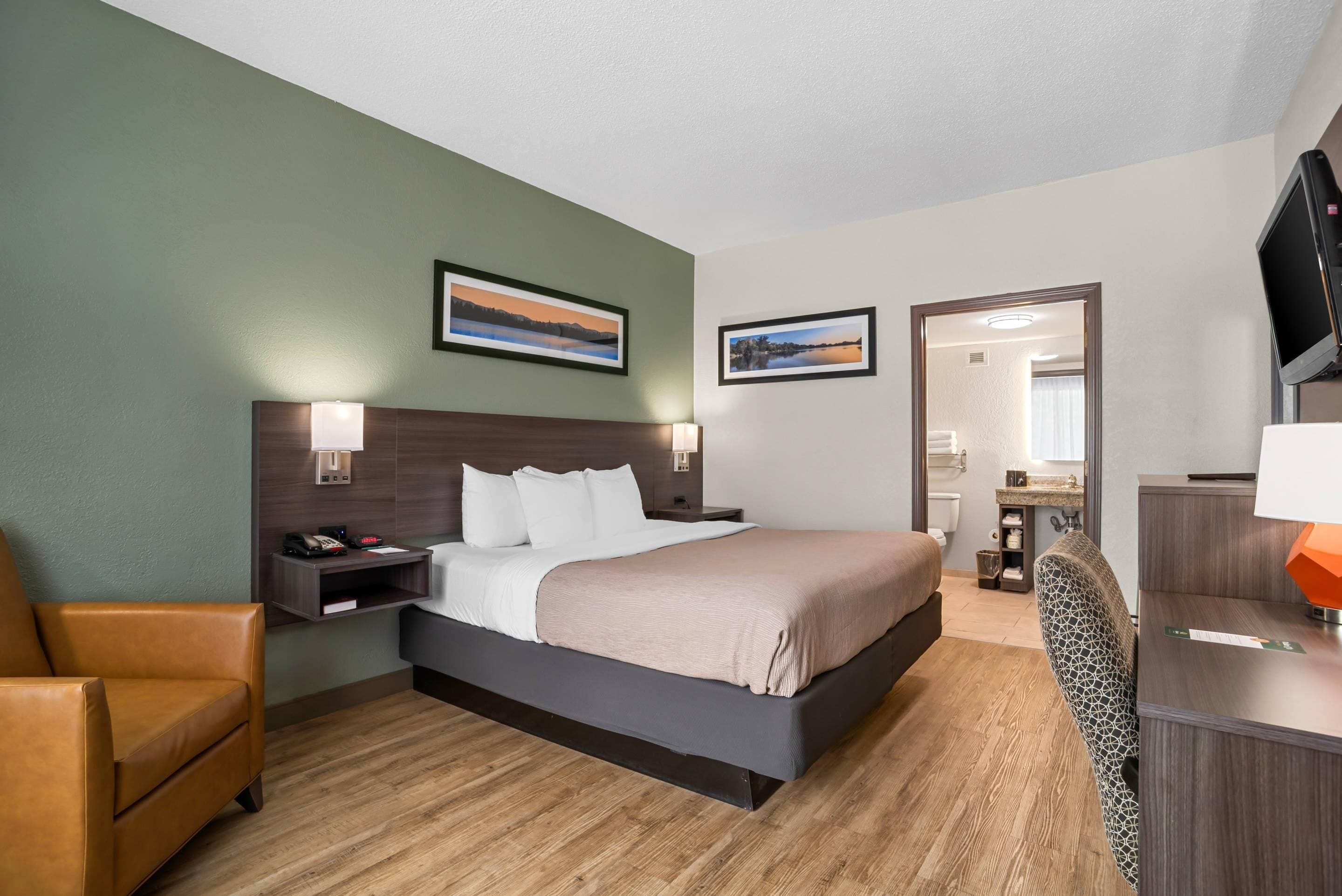 A hotel room with a bed, a chair, a desk, a TV, and two framed pictures on the wall.