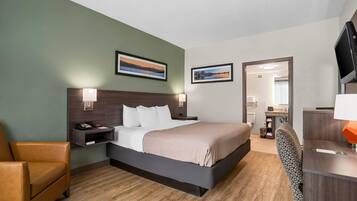 A hotel room with a bed, a chair, a desk, a TV, and two framed pictures on the wall.
