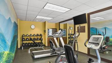Uma academia com equipamentos de exercício, um relógio de parede e um espelho.