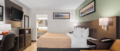 Habitación de hotel con cama, escritorio, silla, televisión y obras de arte en las paredes.