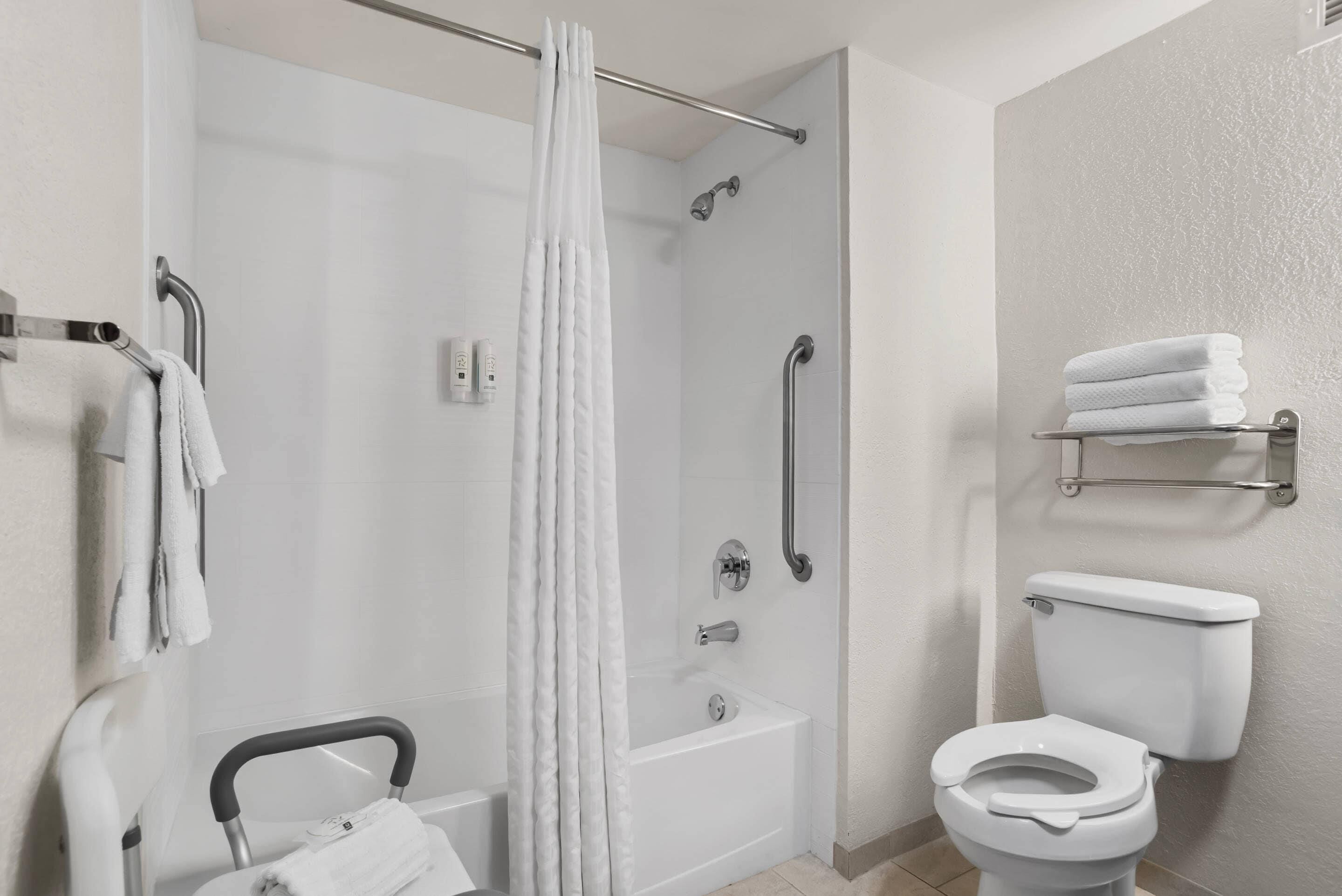A bathroom with a shower, toilet, and grab bars.