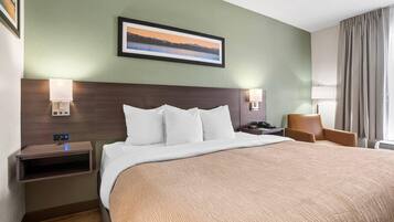 Una camera d'albergo con un letto grande, un comodino, una lampada, una sedia e un quadro appeso al muro.