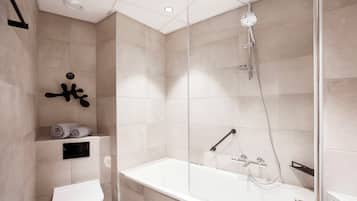 Een moderne badkamer met toilet, douche met glazen cabine en een bad.