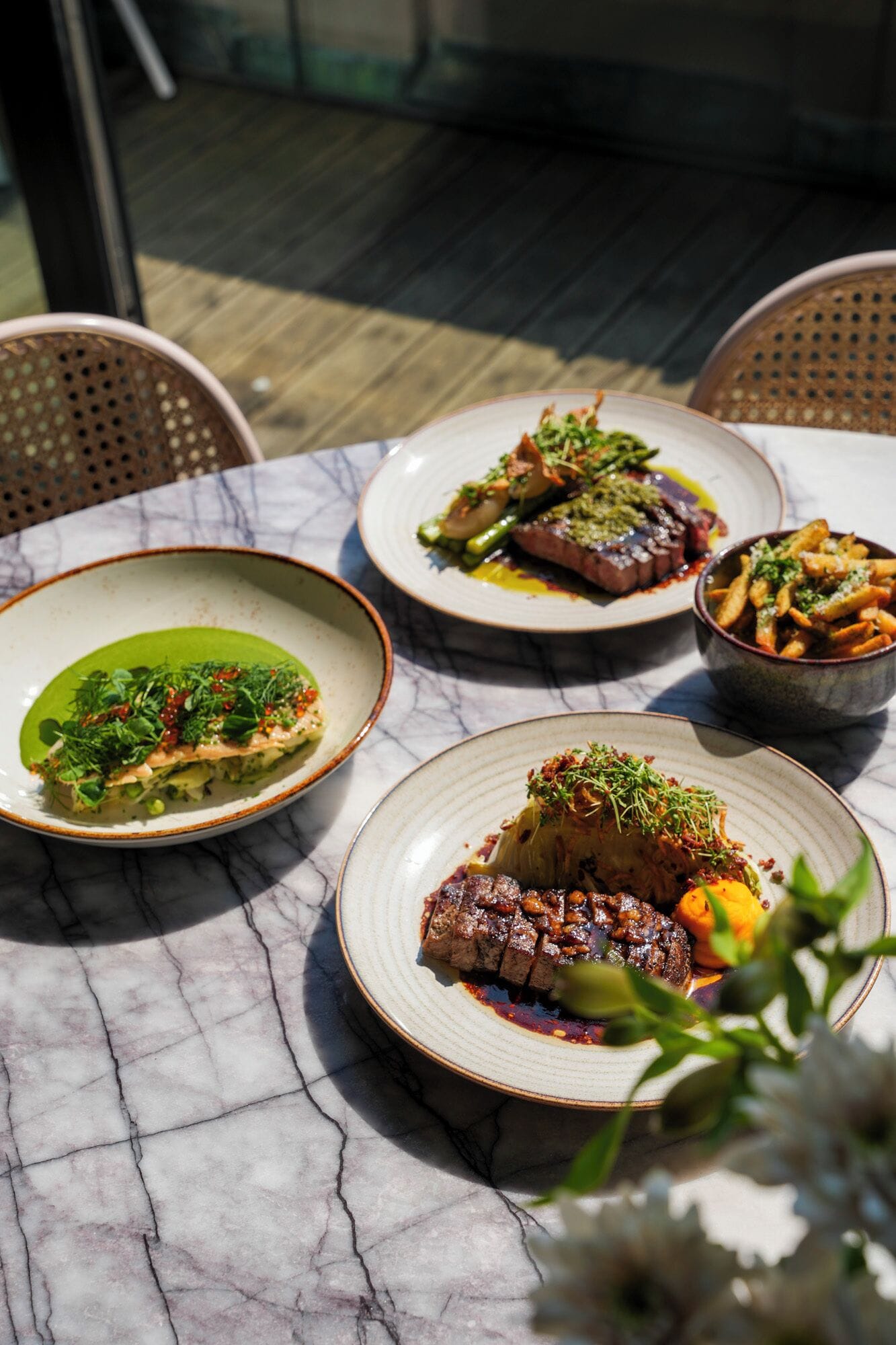 A table with plates of food, a chair, and a glass window in the background.