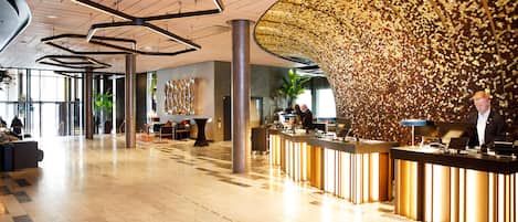Een ruime lobby met een receptiebalie, moderne verlichtingsarmaturen en een decoratieve wand.