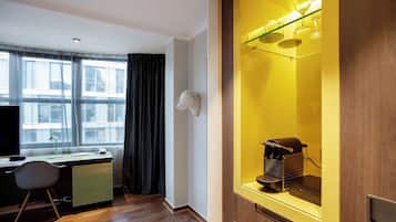 Una habitación de hotel moderna con un escritorio de madera, una silla, un televisor, un ventanal con cortinas y un minibár con cafetera.