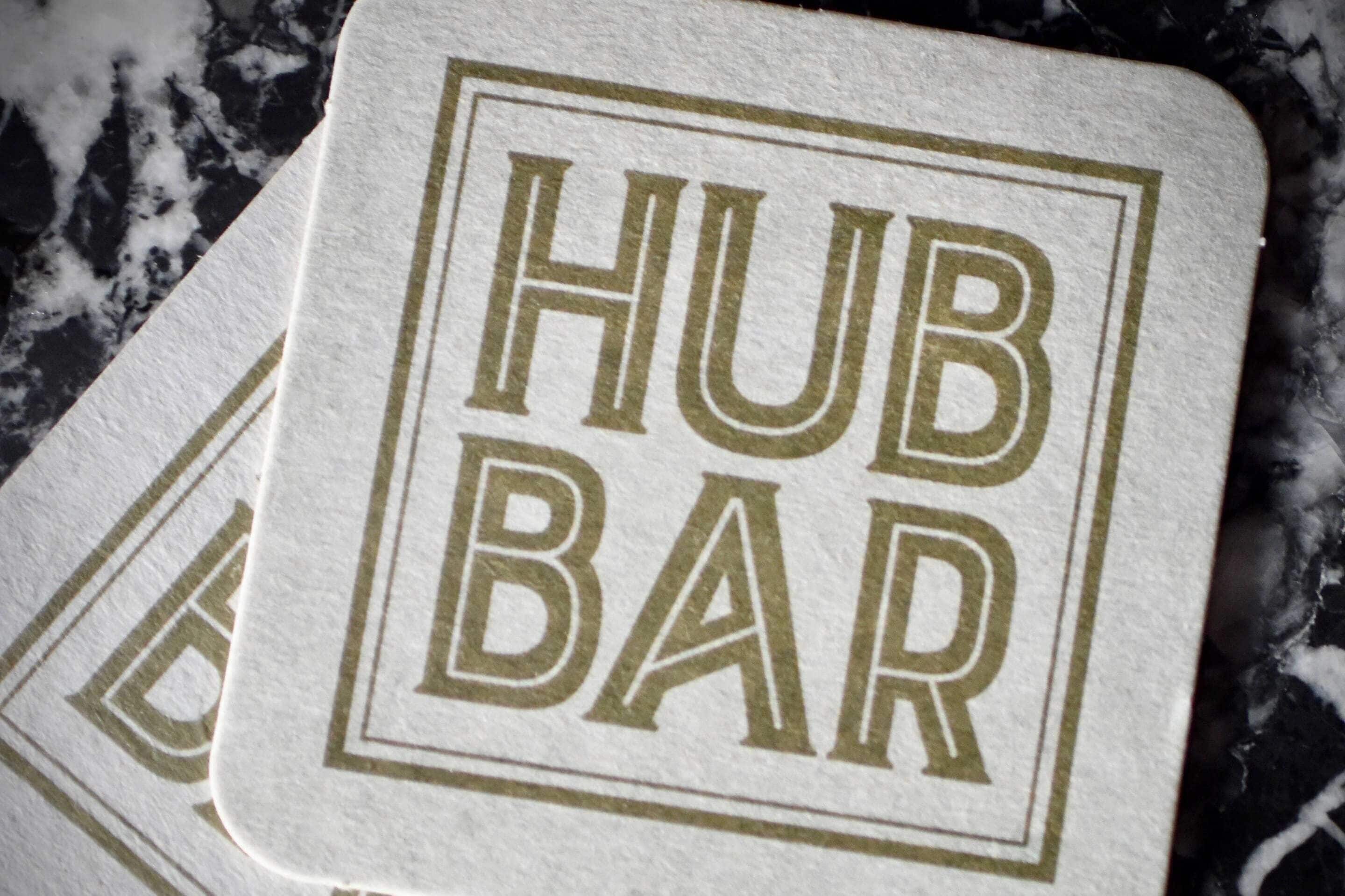 A white coaster with 'HUB BAR' printed in gold.