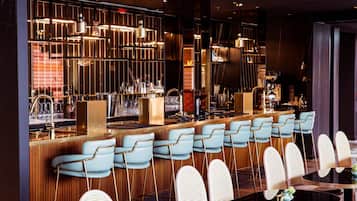 Zona de bar con diversas opciones de asientos, incluyendo taburetes y mesas redondas, con diseño moderno e iluminación ambiental.