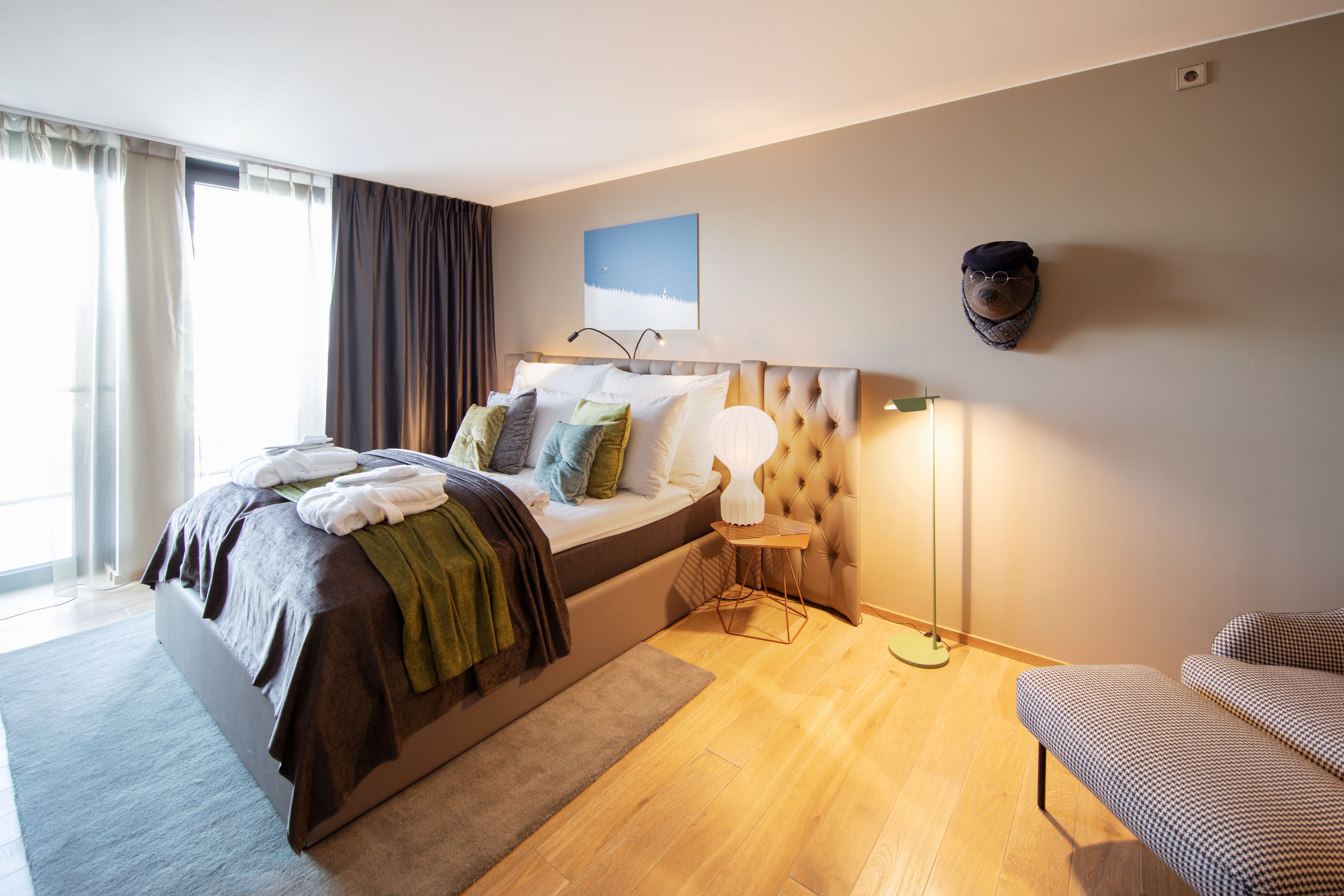 Quarto moderno com uma cama grande, uma mesa de cabeceira com abajur, cabeceira e vista para o exterior pela janela.