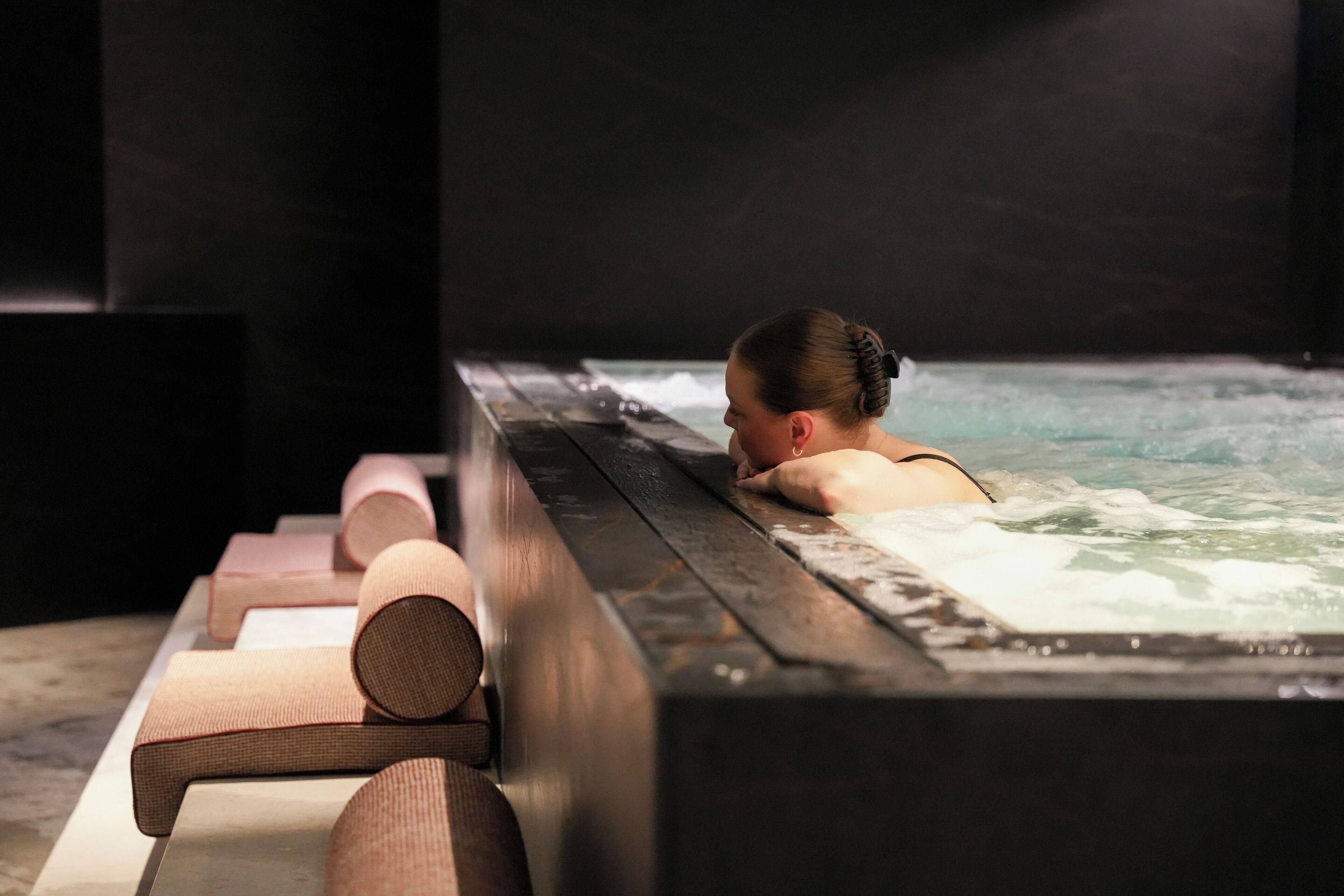 A person relaxing in a hot tub with wooden loungers.