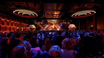 Un espacio interior lleno de gente, con un escenario y una gran audiencia.