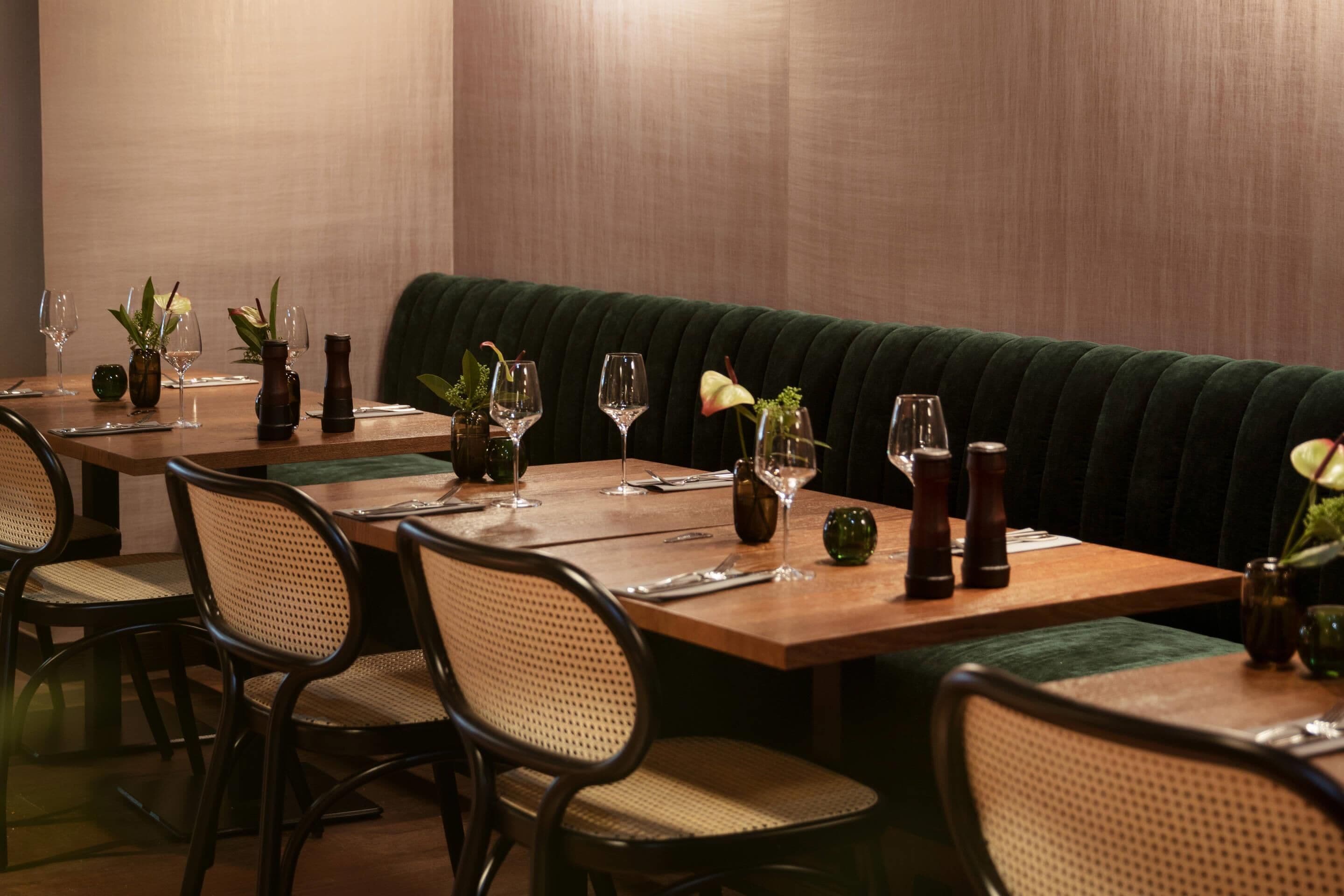 Un restaurant avec une table en bois dressée pour le repas, des sièges rembourrés et des vases décoratifs.