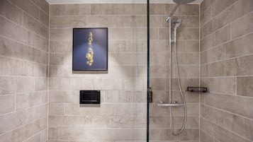 A modern bathroom with beige tiles, a framed artwork, a glass shower enclosure, and a control panel.
