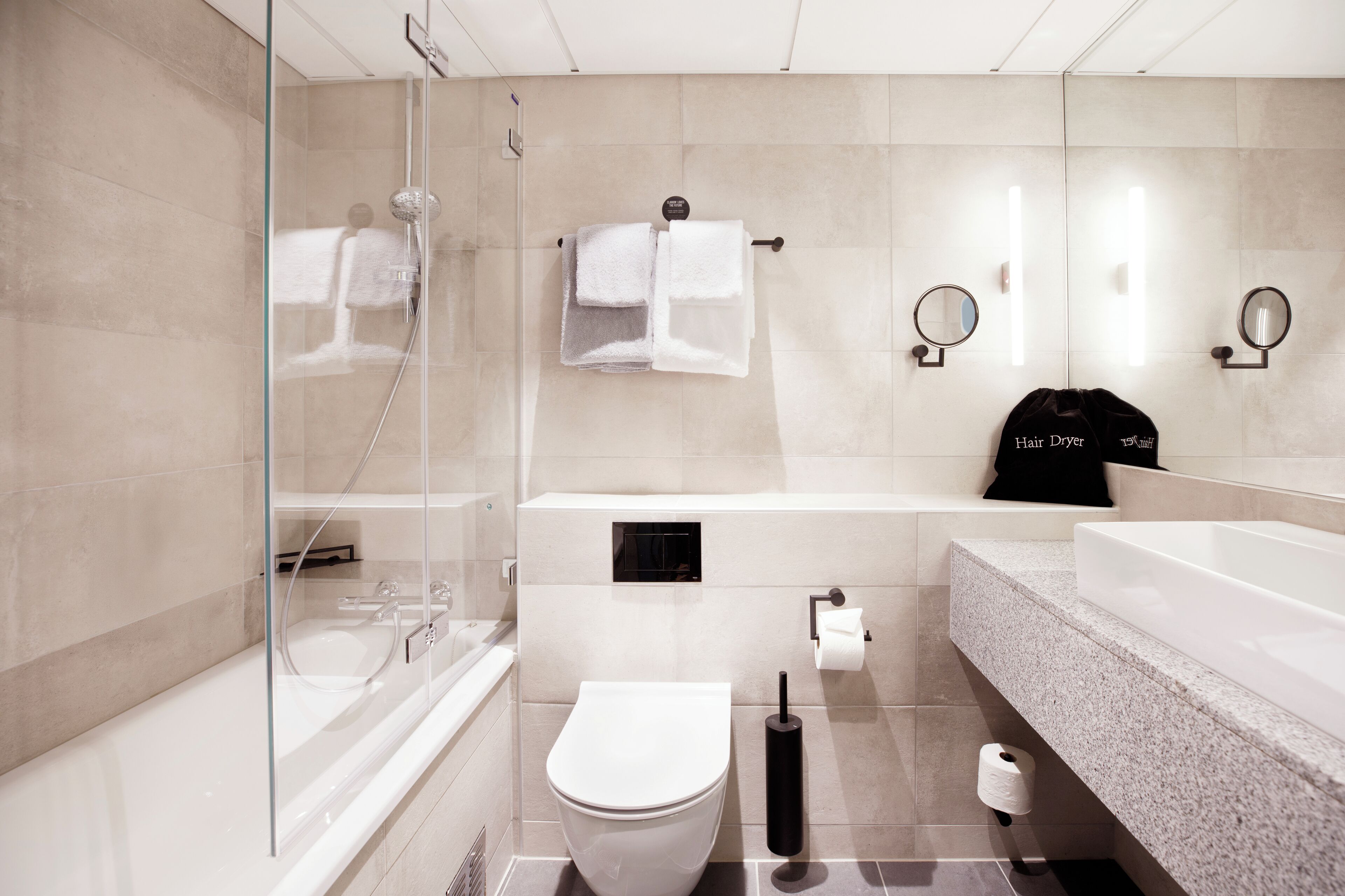A modern bathroom with a glass shower enclosure, a white toilet, a bathtub, and a large sink with a granite countertop.