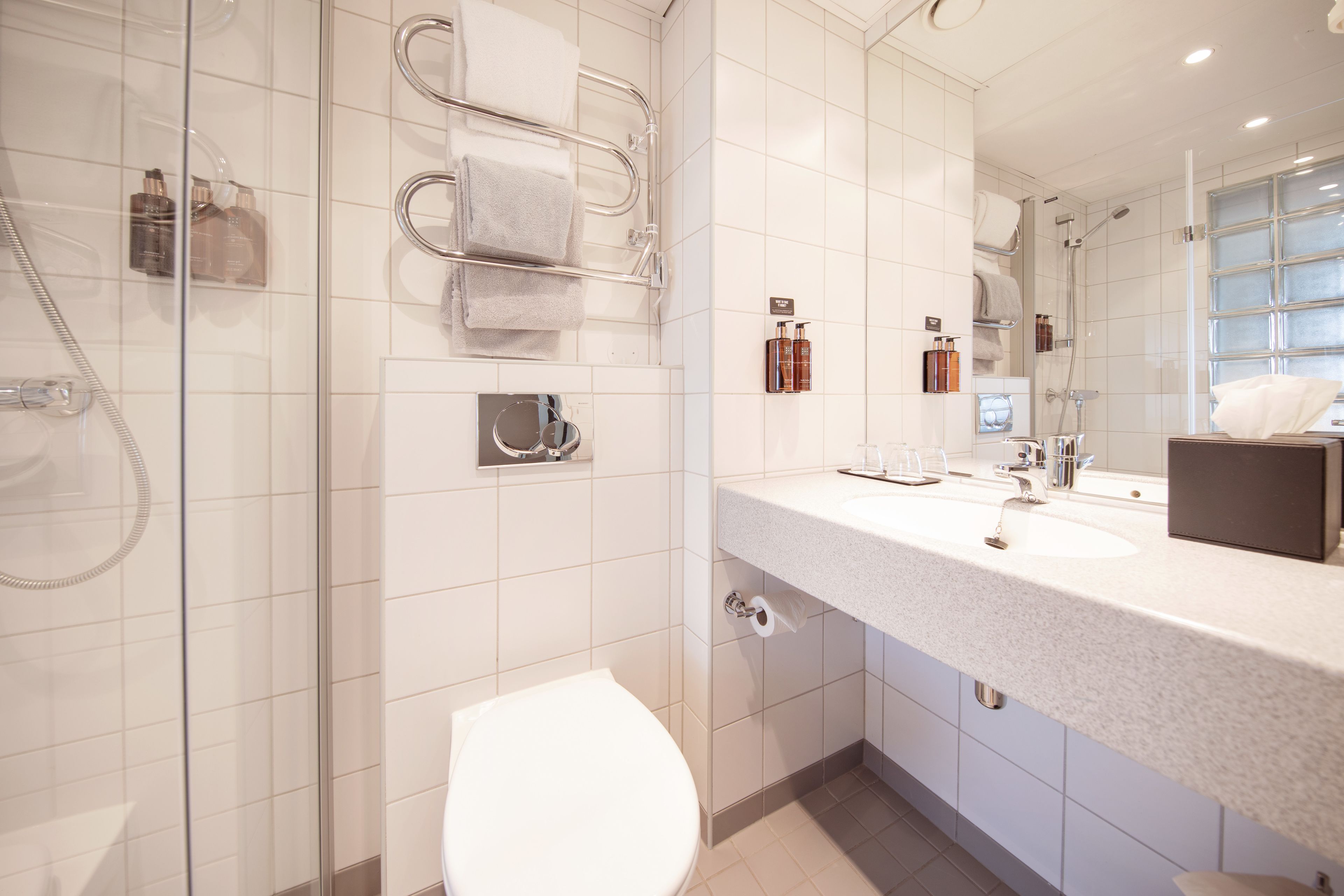 Een moderne badkamer met een douchecabine van glas, een wit toilet, een groot wastafelmeubel met spiegel en netjes opgeruimde toiletartikelen.