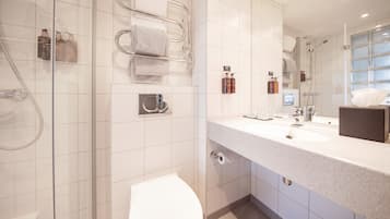 Een moderne badkamer met een douchecabine van glas, een wit toilet, een groot wastafelmeubel met spiegel en netjes opgeruimde toiletartikelen.