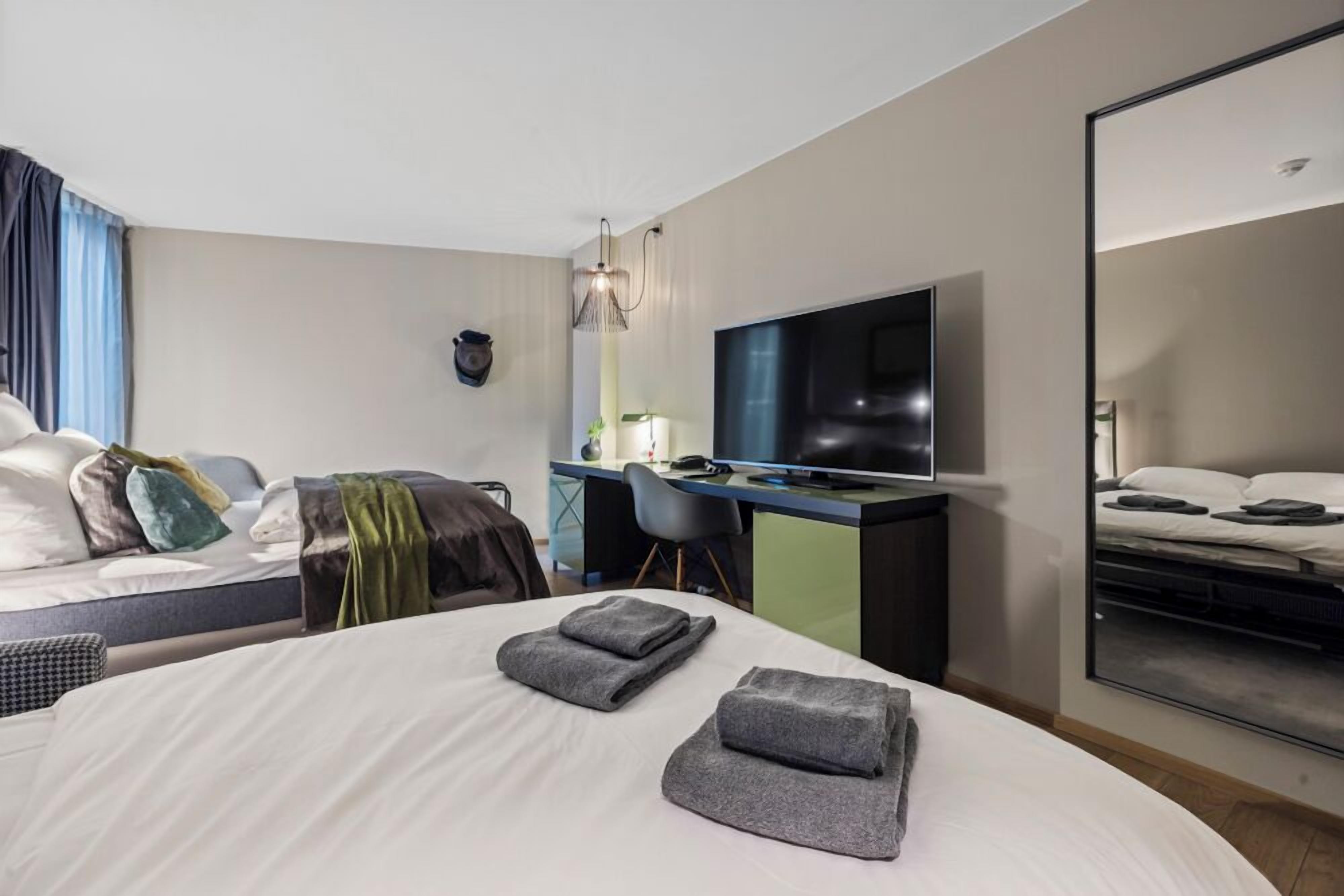 Habitación de hotel moderna con una cama grande, un escritorio, un televisor de pantalla plana y un espejo amplio.