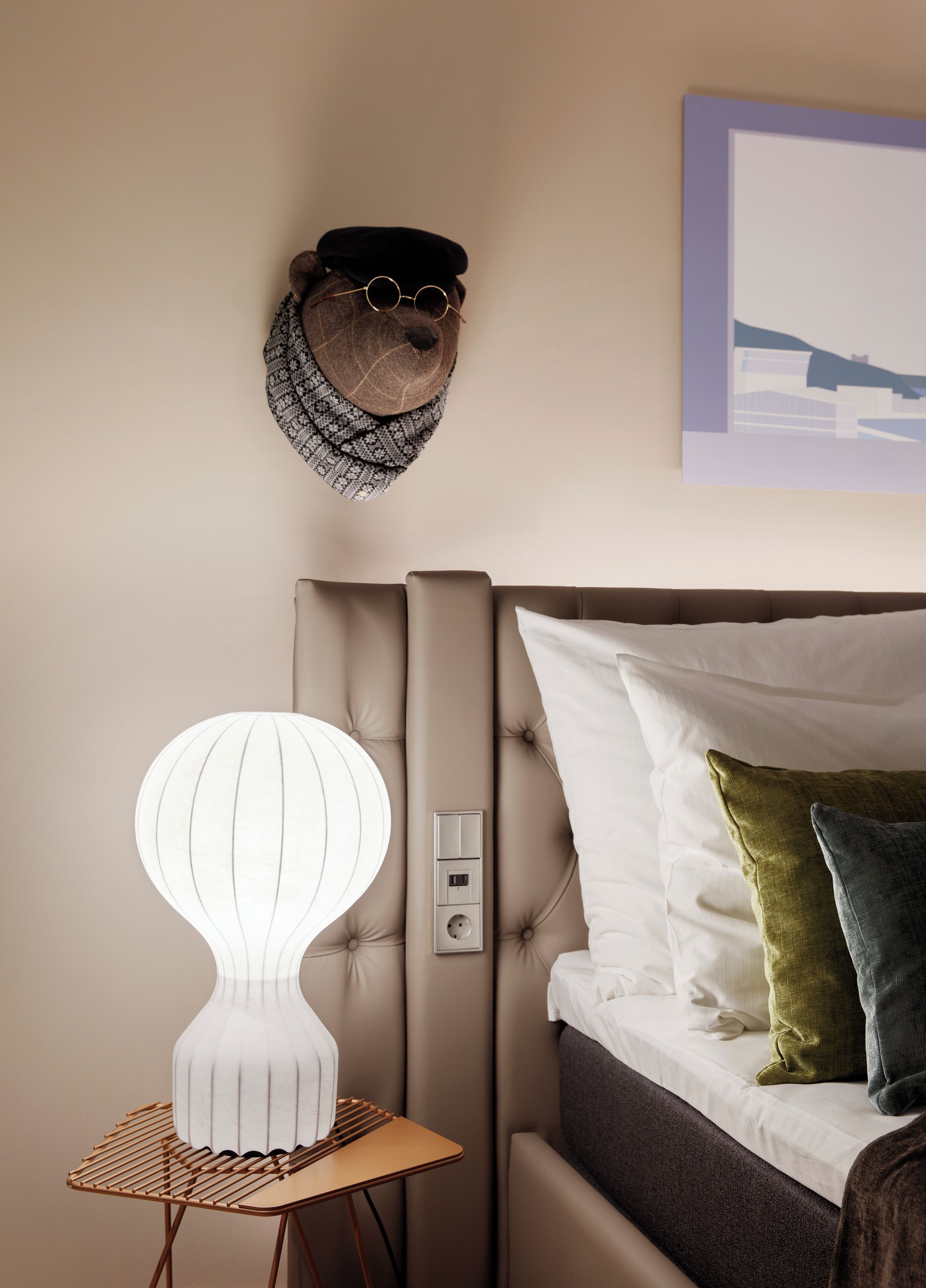 Um quarto com cabeceira estofada, abajur, relógio de parede e quadro emoldurado.