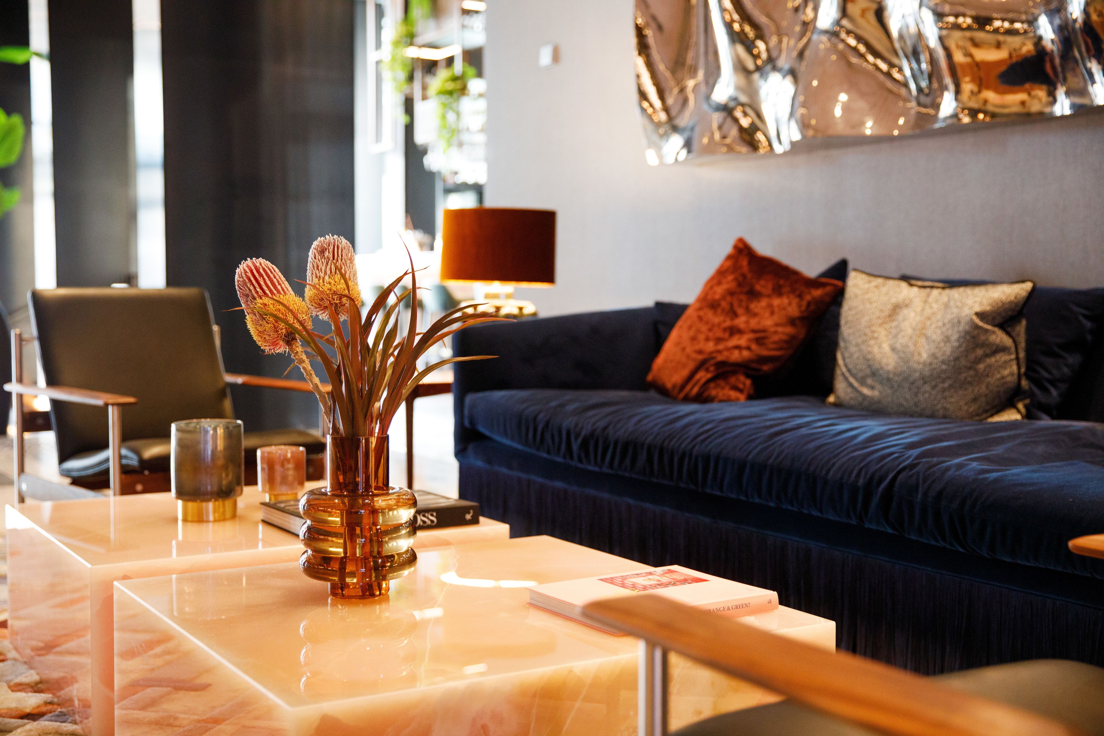 A modern living room with a blue sofa, a coffee table with a vase, and a lamp.
