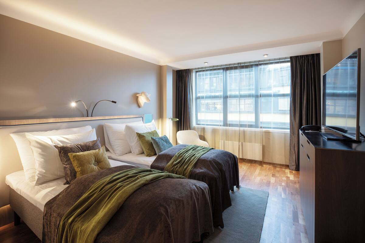 A hotel room with two beds, a desk, a chair, and a large window with curtains.
