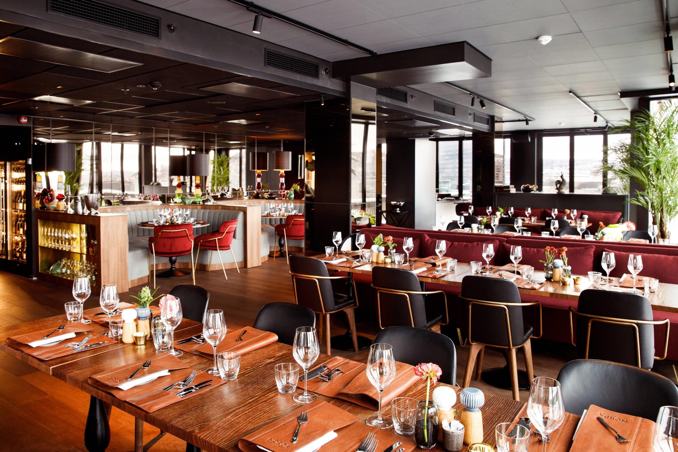 Een restaurant met houten tafels, zwarte stoelen en een bar.