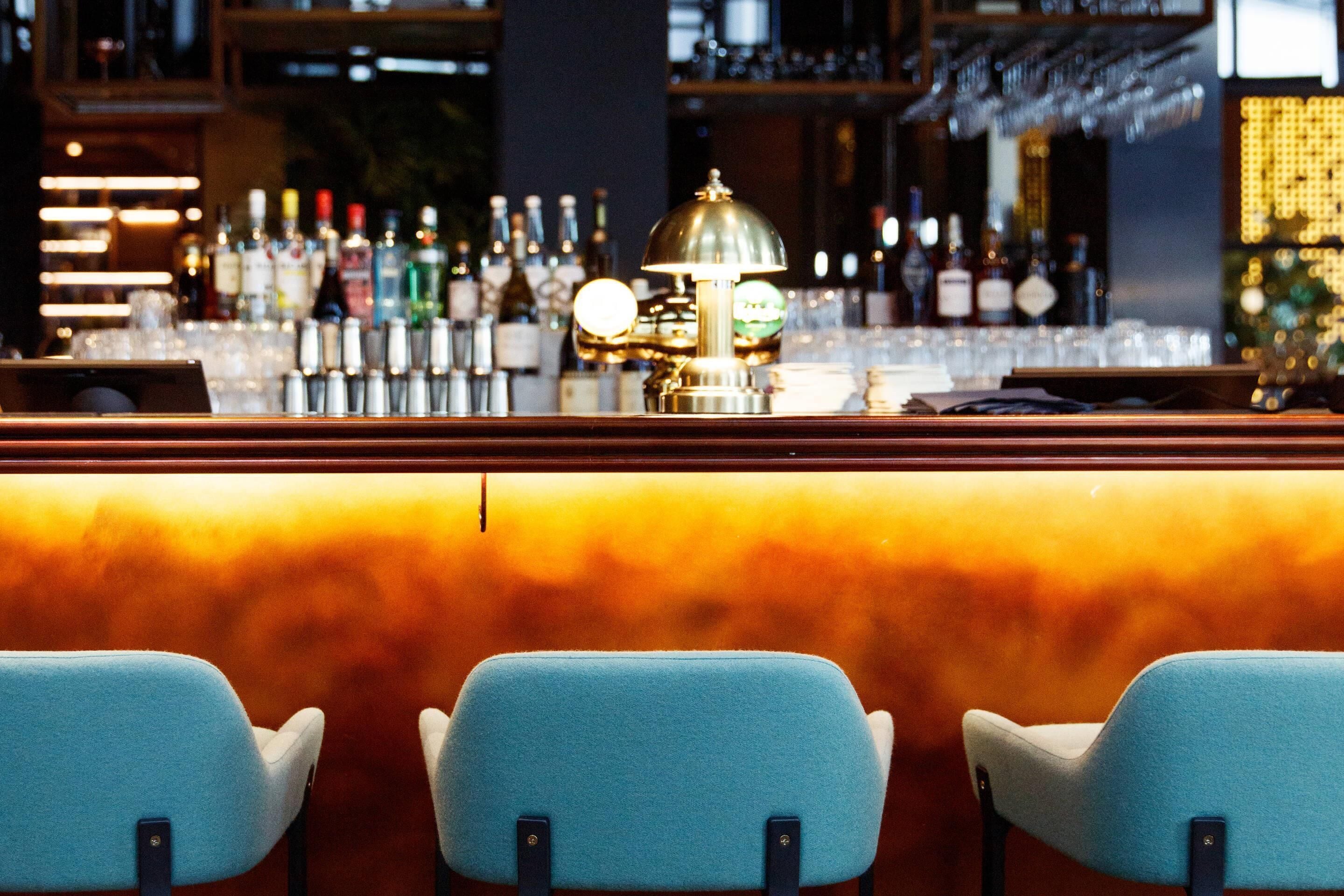 Een bar met een toonbank, barstoelen en diverse flessen en glazen.