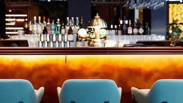 Zona de bar amb taulell, tamborets i una varietat de botelles i gots.