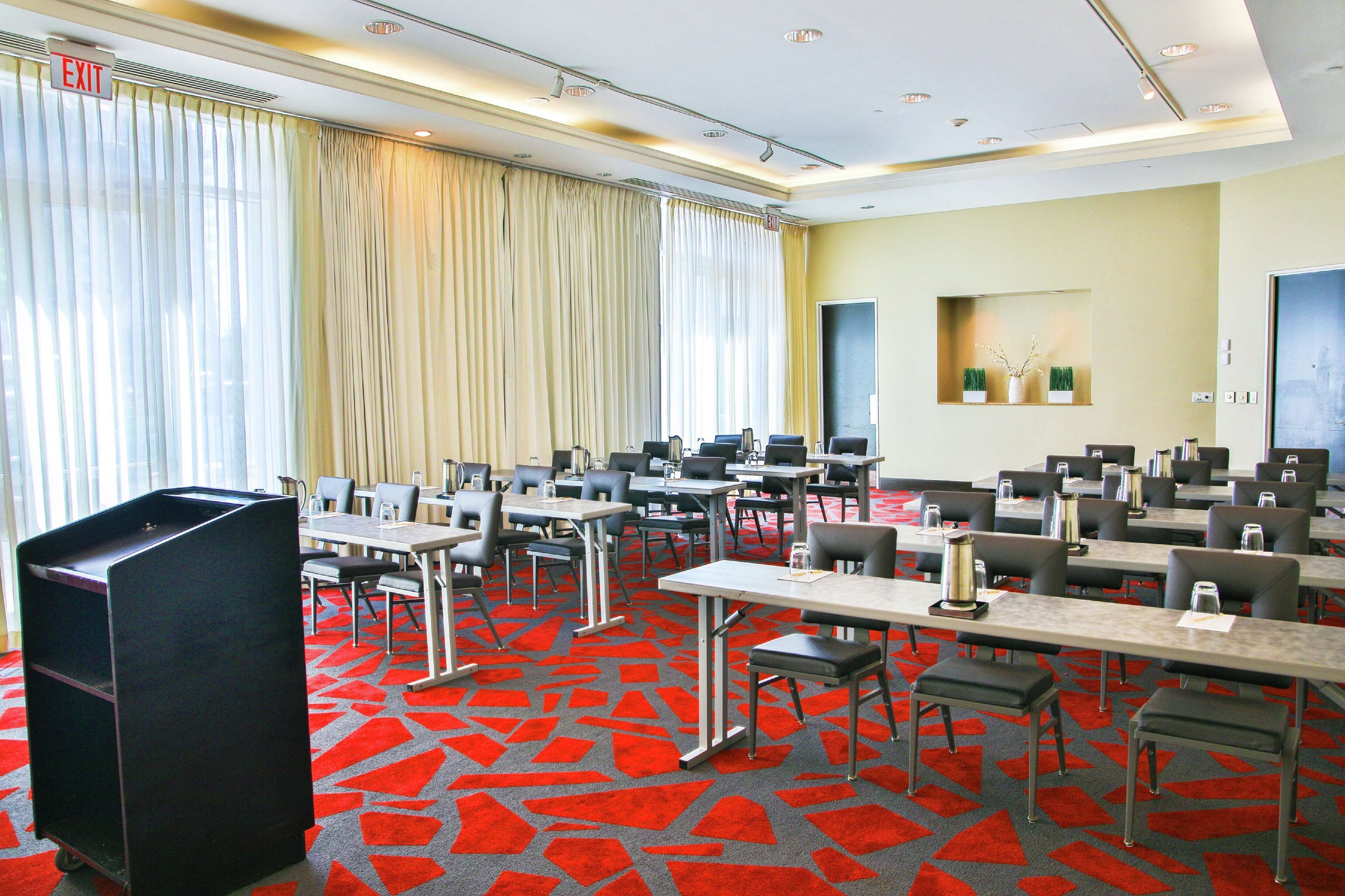 A conference room with multiple tables and chairs, a podium, and a large window with curtains.