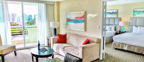 Habitación de hotel con sofá, cama, mesita de vidrio y vistas de la ciudad.