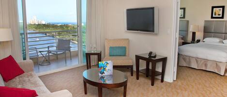 A hotel room with a balcony, a bed, a TV, a desk, and a sofa.