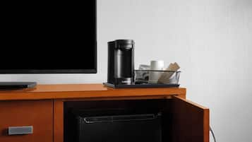 Una kitchenette con cafetera, una cesta con tazas y un televisor de pantalla plana sobre una encimera de madera.