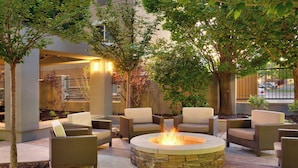 An outdoor patio area with wicker furniture, a stone fire pit, and trees providing shade.