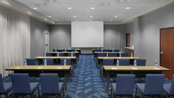 A conference room with multiple tables and chairs, a projector screen, and a water dispenser at each table.