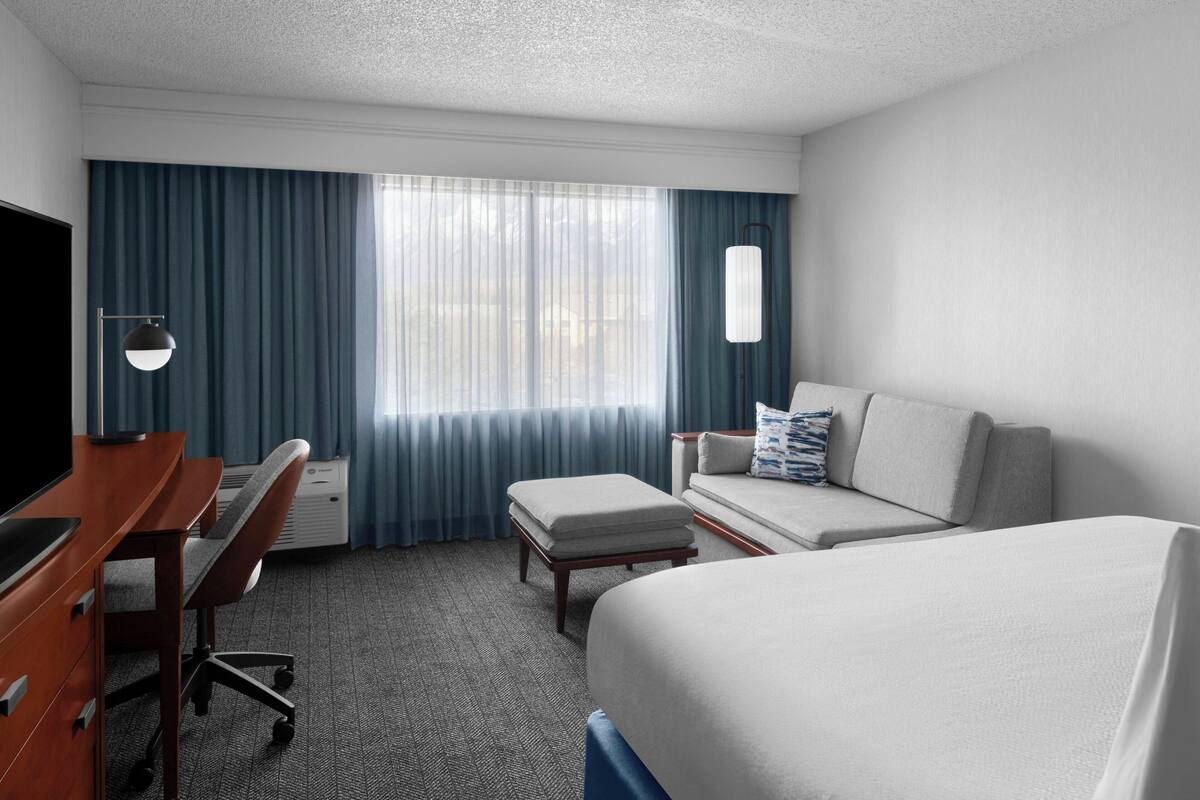 A hotel room with a bed, a desk, a chair, a sofa, and a TV.