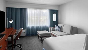 Habitación de hotel con cama, escritorio, silla, sofá y televisor.