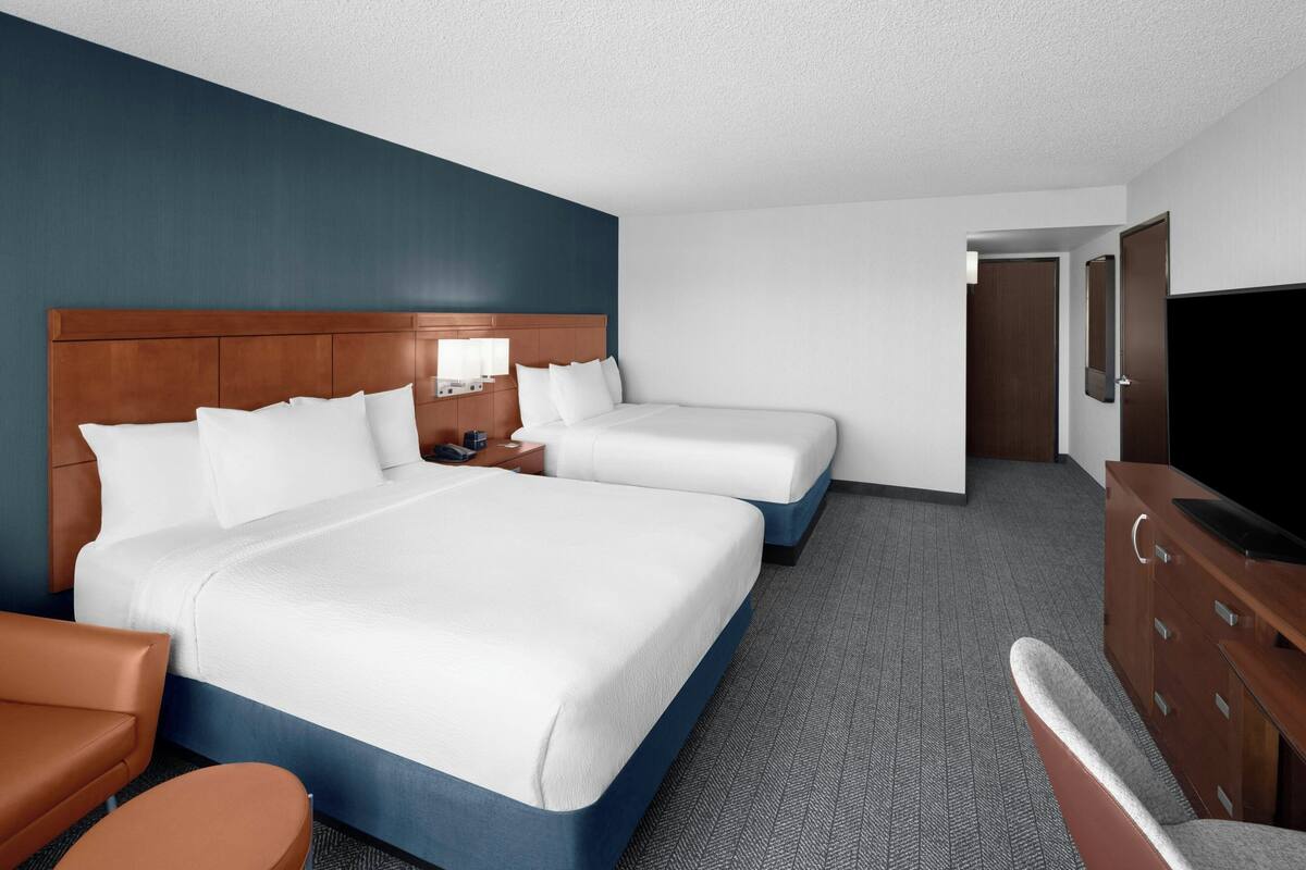 A hotel room with two beds, a desk, a chair, a TV, and a wardrobe.