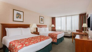 A hotel room with two beds, a desk, a chair, a TV, and a window with curtains.