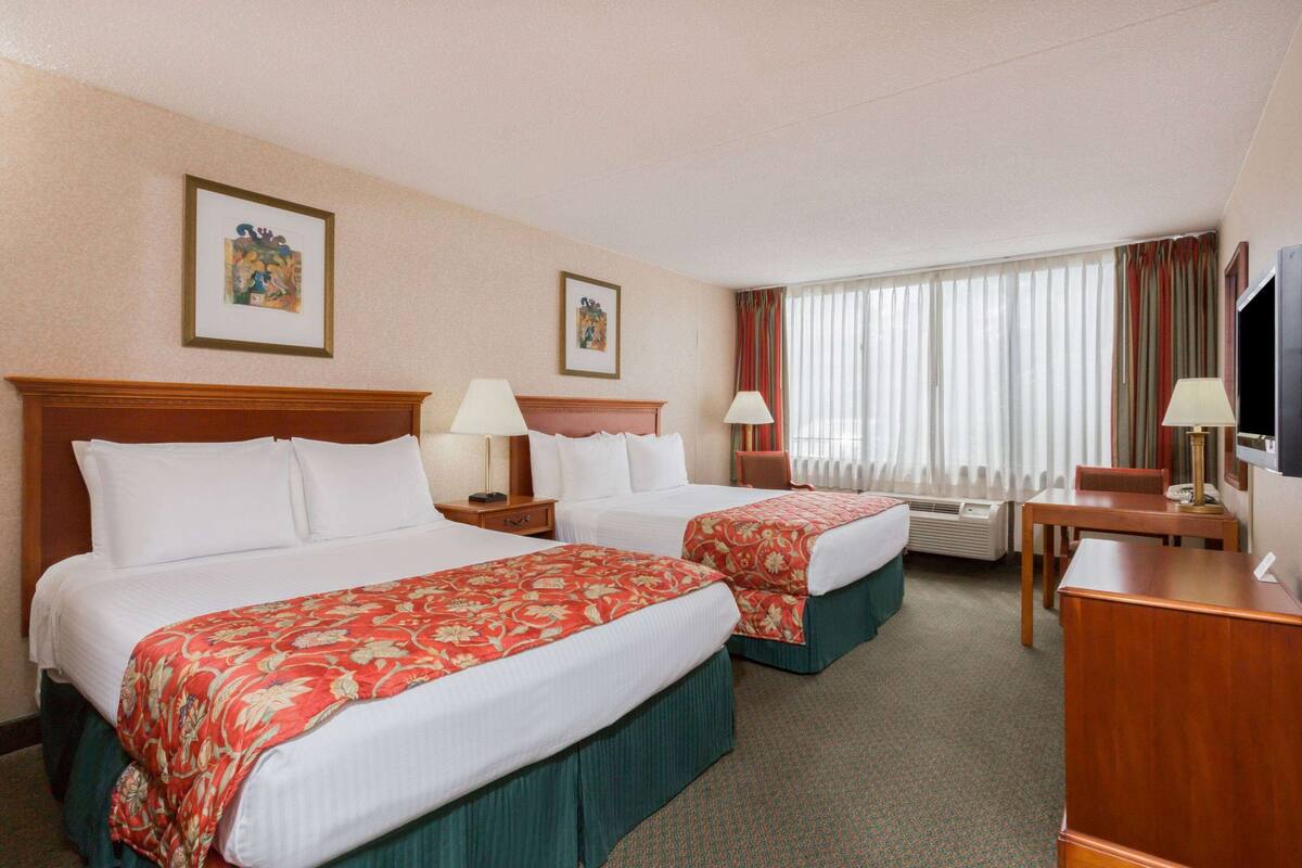 A hotel room with two beds, a desk, a chair, a TV, and a window with curtains.
